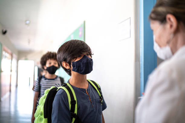 istock Student arriving in classroom and talking to teacher - using protective face mask 1367325987
