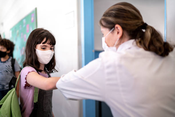 istock Kids greeting teacher with an elbow bump in the classroom - using a face mask 1367326781