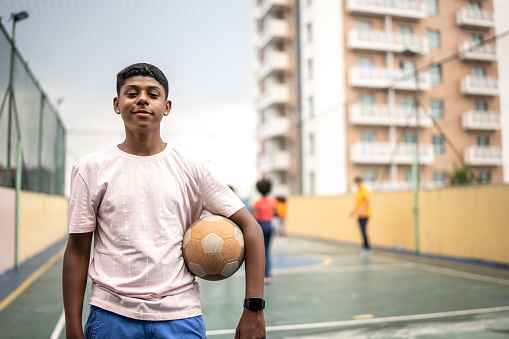 Portrait of a boy holding a ball at a sports court
