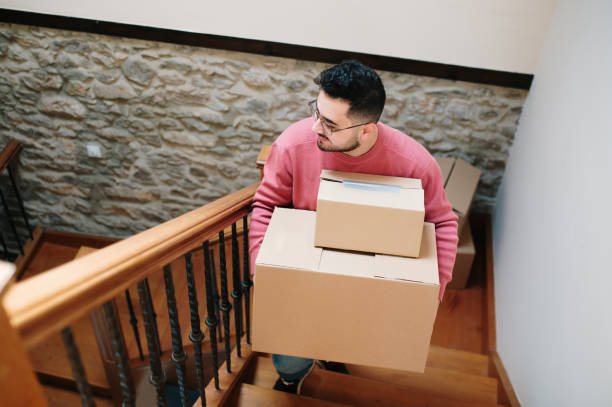 istock Young man going up a staircase with cardboard boxes 1367328450