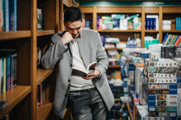 istock Young man-student reading book between the shelves in the library 1367328472