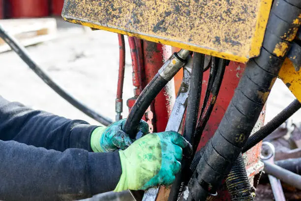 Photo of Worker is repairing hydraulic pipes of working machine. Hydraulic machines use liquid fluid power to perform work. Heavy construction vehicles are a common example.