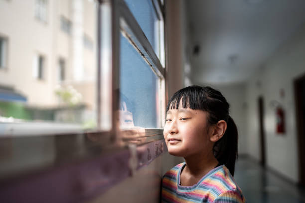 istock Contemplative girl looking through the window at school 1367329966