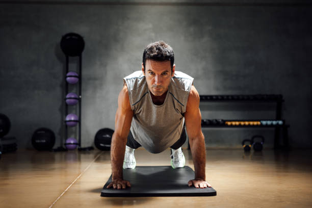 istock Sportsman bodybuilder does push-ups while looks at camera in a dark gym. 1367330004