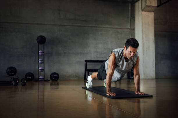 Athletic man doing pushups exercise at dark gym. Athletic man doing pushups exercise in sportswear, trains doing plank pose at dark gym floor, looking down, indoors. Dramatic dark shadow background. Copy-space. push ups stock pictures, royalty-free photos & images