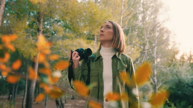 Girl in nature with vintage camera looking at trees at sunset, medium shot, slow motion, handheld.