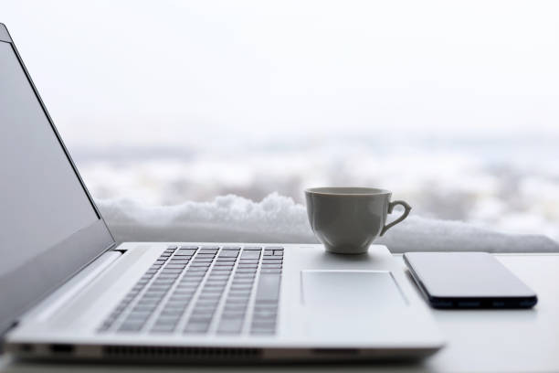 Coffee cup and laptop on table against the window, view to winter city during snow stock photo