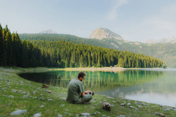 Male traveler with dog contemplating sunrise at the scenic mountain lake in Montenegro Happy man in eyeglasses and his dog - pug breed sitting by the picturesque Black Lake with view of the mountains and pine forest in Durmitor National park man walking a pug dog stock pictures, royalty-free photos & images