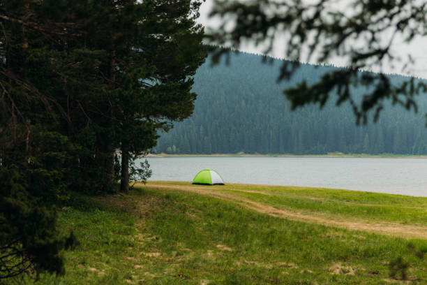 Scenic view of the tent on the green meadow by the beautiful Black Lake with view of the mountain peak and pine forest in Durmitor National park, Montenegro