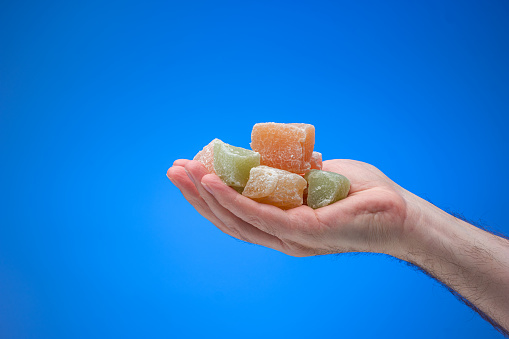 Cubes of colored Turkish Delight held in male hand. Close up studio shot, isolated on blue background.