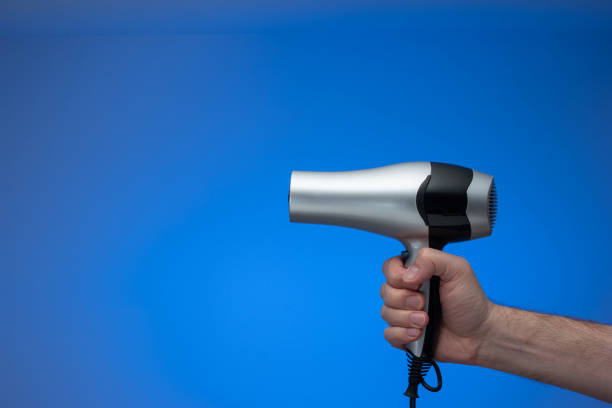 ogólna srebrna suszarka do włosów trzymana w ręku przez kaukaskie męskie ramię. zbliżenie studyjne, izolowane na niebieskim tle, bez ludzi - hair dryer single object plastic black zdjęcia i obrazy z banku zdjęć