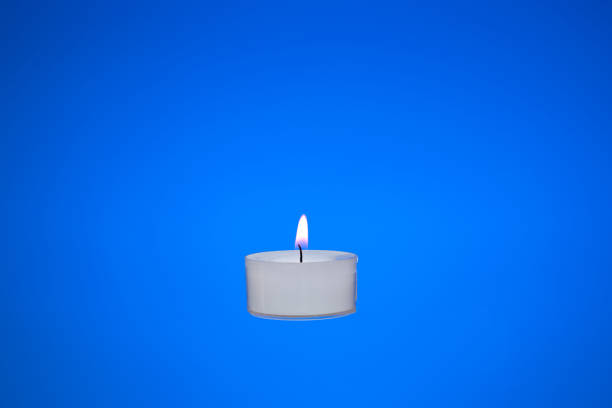 Single small white candle burning. Close up studio shot, isolated on blue background.