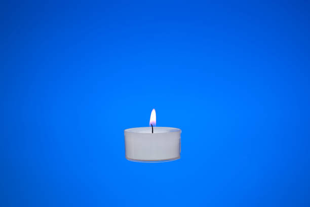 одна маленькая белая свеча горит. студийный снимок крупным планом, изолированный на синем фоне - tea light candle white single object стоковые фото и изображения