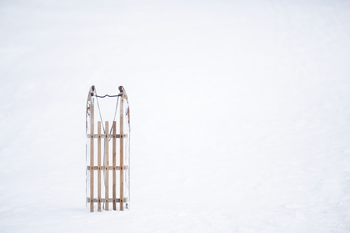 Old wooden sledge on white fresh snow background in winter day. Front view. Empty place for text.