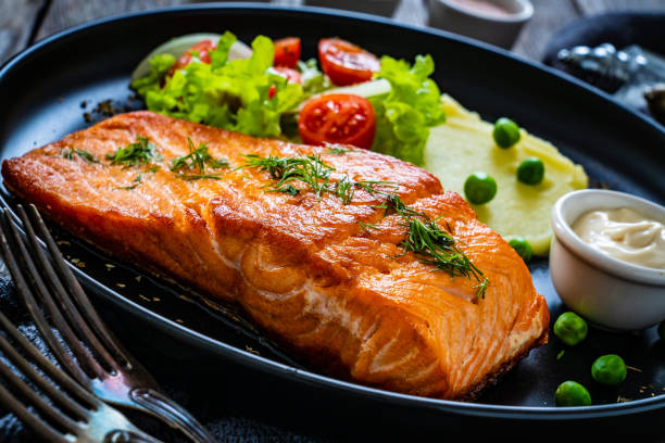 istock Fried salmon steak and fresh vegetables on black wooden background 1367341875