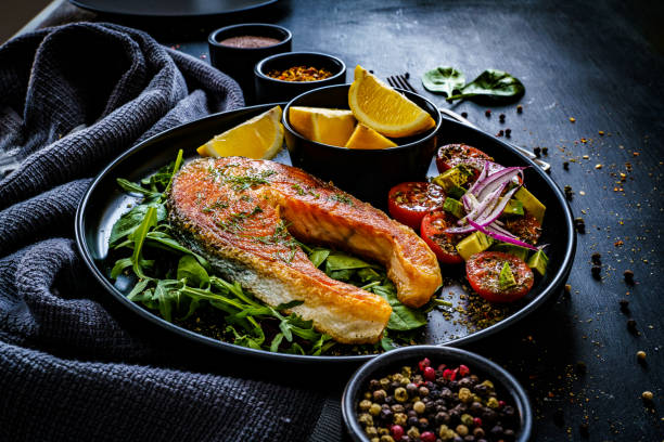 istock Fried salmon steak and fresh vegetables on black wooden background 1367342019
