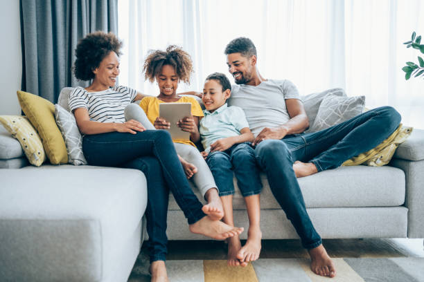 Relaxing at home with wireless technology. Shot of a smiling family with two kids using digital tablet on the sofa at home. family dependency mother family with two children stock pictures, royalty-free photos & images