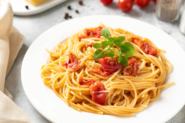istock Spaghetti with tomatoes, parmesan and basil in a white plate on a bright kitchen table. Traditional Italian pasta with vegetables and cheese 1367343276
