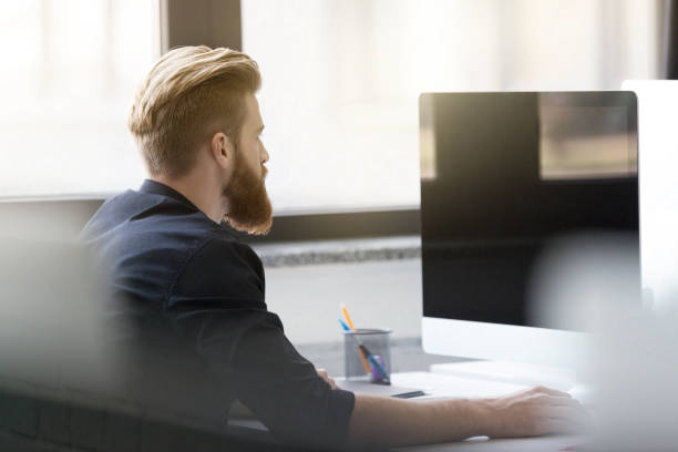 istock Young bearded man sitting at his desk 1367343576