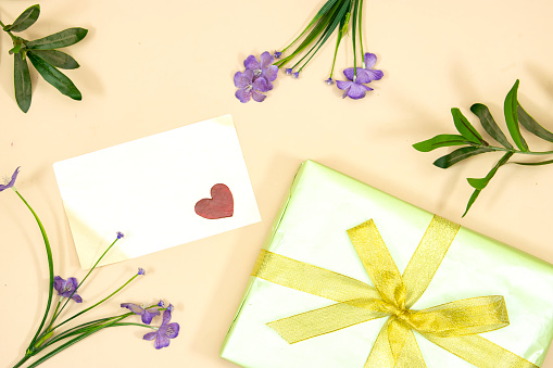 happy valentine's or mother's day concept. empty card and small red wooden heart on gift decorated with yellow ribbon and flowers isolated on pink background