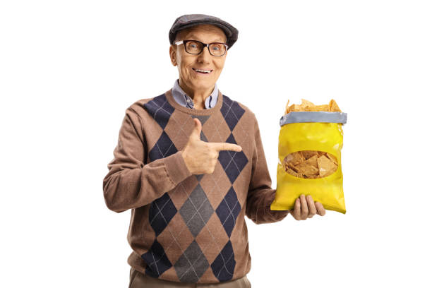 istock Cheerful elderly man holding a pack of tortilla chips and pointing 1367344658