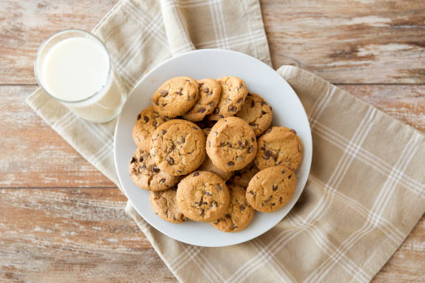 close up of oatmeal cookies and glass of milk food, junk-food and eating concept - close up of oatmeal cookies with chocolate chips and glass of milk on plate chocolate chip cookie top view stock pictures, royalty-free photos & images