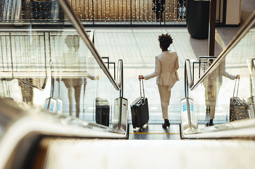 Happy businesswoman holding wheeled suitcase in airport during the day.