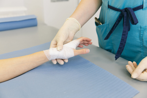 A doctor wrapped around the wrist for first aid close-up. Application of bandages on the patient's hands, first aid concepts and wrist injury treatment. Medical bandage on patient hand. Wrist pain.