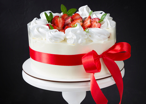 White cake with strawberry and red ribbon, black background. Valentine's day, birthday cake background