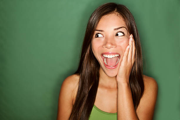 amazement - woman excited looking to the side amazement - woman excited looking to the side. Surprised happy young woman looking sideways in excitement. Mixed race Chinese Asian / white Caucasian female model on green background. See more: sideways glance stock pictures, royalty-free photos & images