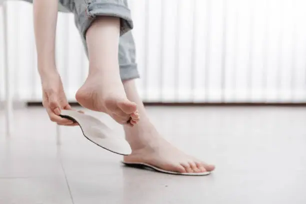 Photo of Woman fitting orthopedic insole indoors, close up. Girl holding an insole next to foot at home. Orthopedic insoles. Foot care banner. Flat Feet Correction. Treatment and prevention of foot diseases