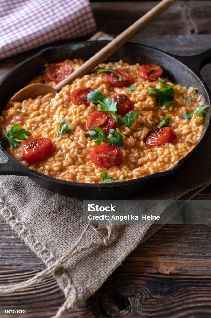 Traditional risotto with parmesan cheese and tomatoes Fresh and homemade cooked tomato risotto with roasted tomatoes and parmesan cheese. Served in a rustic cast iron pan on wooden table. Closeup, Vertical image with copy space Risotto Stock Photo