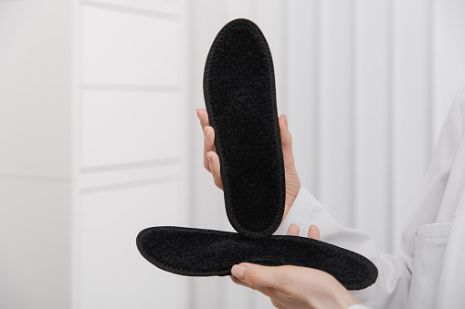 Doctor holding orthopedic insoles in his hands. Orthopedist tests the medical device. Orthopedic insoles on a white. Foot care. Flat Feet Correction. Prevention of flat feet and foot diseases.