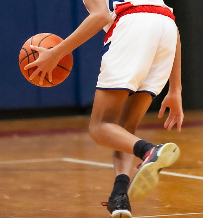 Rear view of a high school basketball player dribbling the ball down the court during a game.