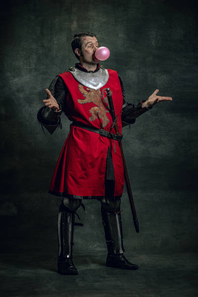 istock One cheerful medieval warrior or knight with dirty face in war equipment having fun isolated over dark background. Comparison of eras 1367355139