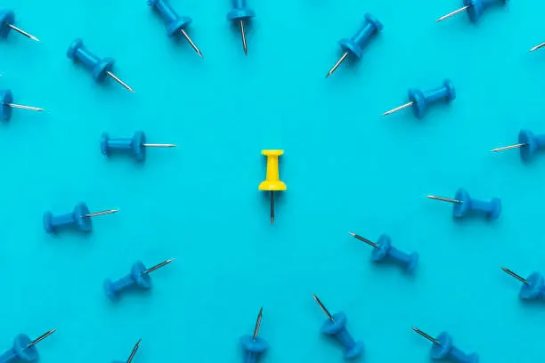 yellow push pin in the center of blue push pins with their spike turned to the yellow one as a concept of bullying or discrimination. conceptual photo of attack on person for opinion or views