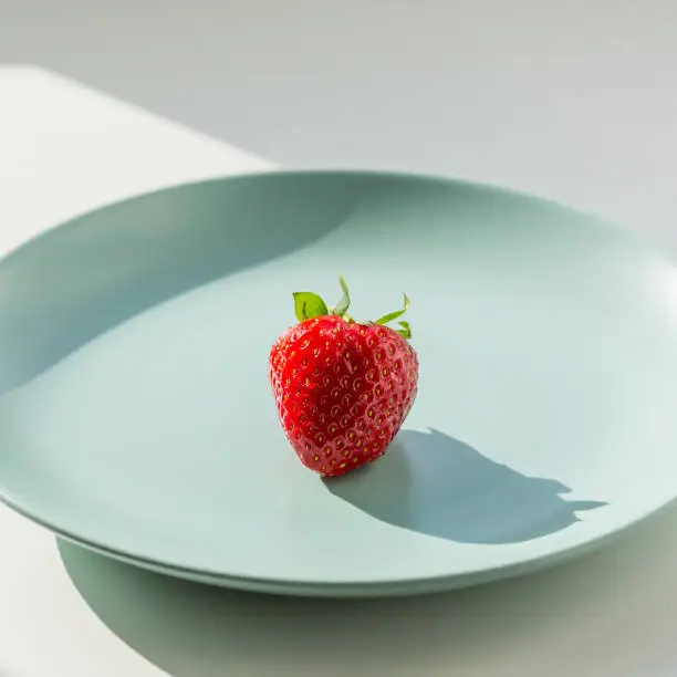 One fresh red ripe strawberry on the green plate. Healthy lifestyle concept.