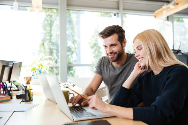 istock Happy young colleagues sitting in office coworking using laptop 1367361353