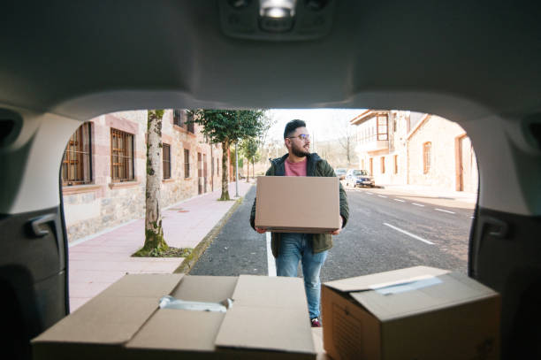 un jeune homme charge une voiture avec des boîtes en carton - moving house physical activity moving van box photos et images de collection