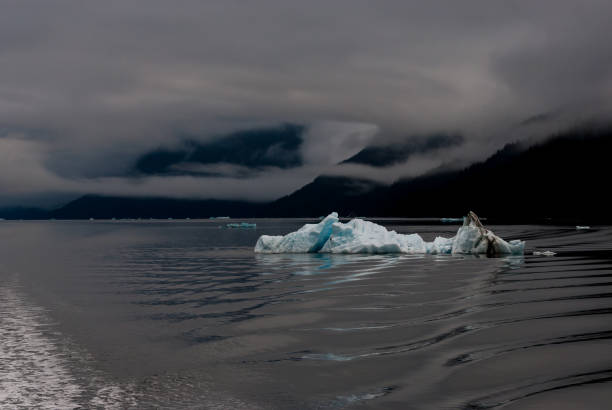 istock Alaska blue iceberg with cloudy mountains behind and wake from ship in front. 1367362032
