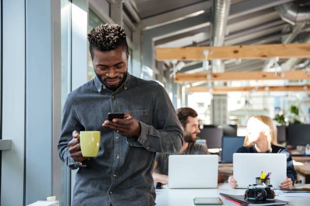 istock Smiling young african man standing in office chatting by phone 1367362456