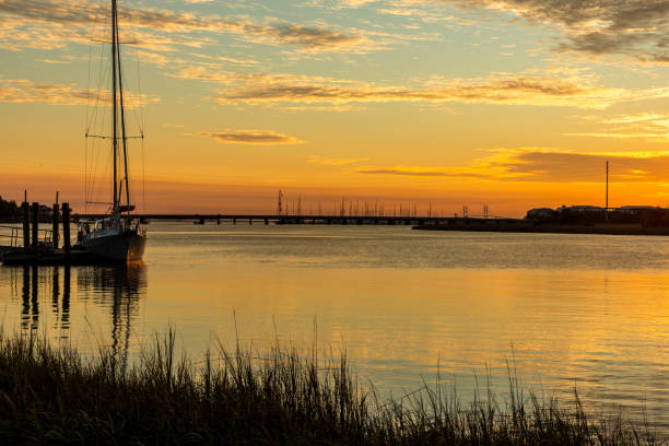 Marsh grasses, a sailboat, bridges and shoreline all stand in silhouette against an intense sunset over the Frederica River adjacent to Georgia's St. Simons Island.