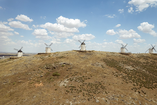 Aerial shot, drone point of view famous windmills in Consuegra town, symbol of Castilla-La Mancha, windmills located on hills against cloudy sky. Heritage, spanish landmarks concept