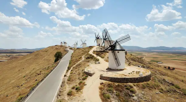 Aerial shot, drone point of view famous windmills in Consuegra town, symbol of Castilla-La Mancha, windmills located on hills against cloudy sky. Heritage, spanish landmarks concept