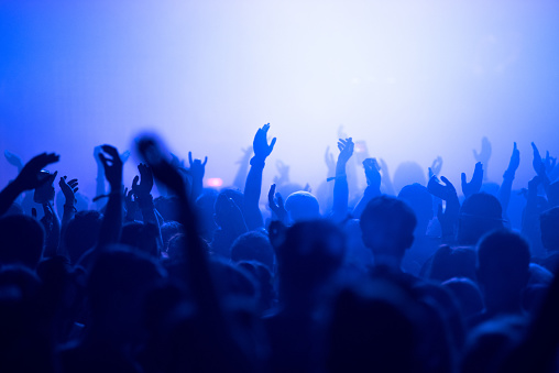 People with raised hands, silhouettes of concert crowd in front of bright stage lights
