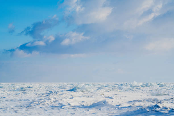The boundless snow-covered fields of the frozen Lake Baikal and light clouds on the blue sky