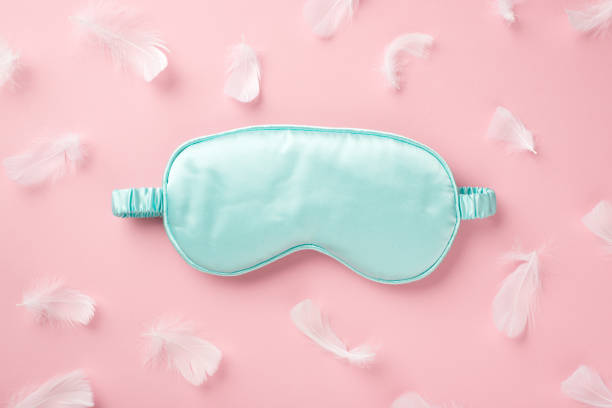 空きスペースを持つ孤立したパステルピンクの背景に水色のシルクの睡眠マスクとピンクの羽のトップビュー写真 - beautiful pink blue lifestyles ストックフォトと画像