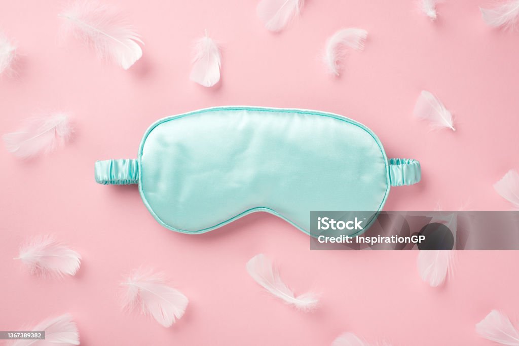 Top view photo of light blue silk sleeping mask and pink feathers on isolated pastel pink background with empty space Eye Mask Stock Photo