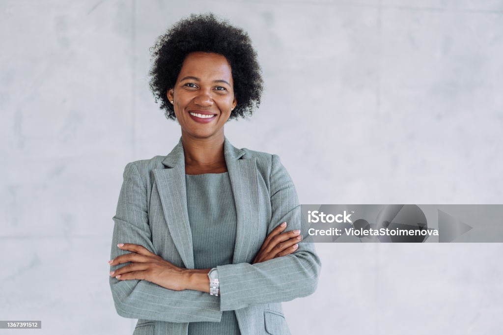Portrait of a smiling young businesswoman. Portrait of beautiful confident smiling african-american businesswoman standing with arms crossed in the office and looking at camera. One Woman Only Stock Photo