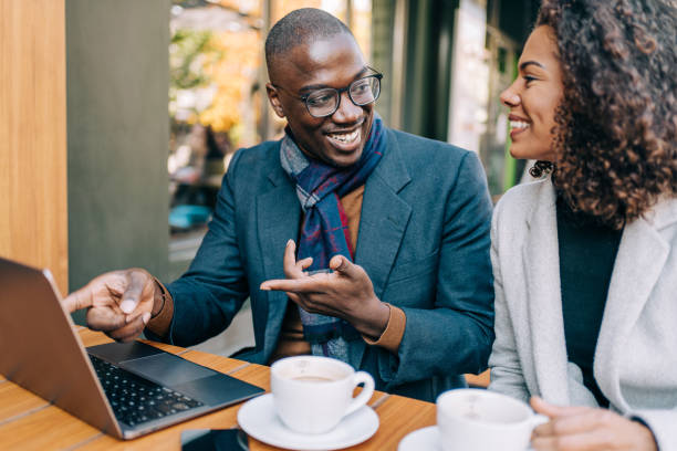 Young couple sitting in a sidewalk cafe and using laptop. Businessman and businesswoman are having a coffee break together in a cafe. african american business couple stock pictures, royalty-free photos & images